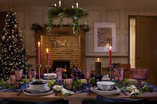 Christmas dinner setting with candles, festive tableware and Christmas tree in the background.